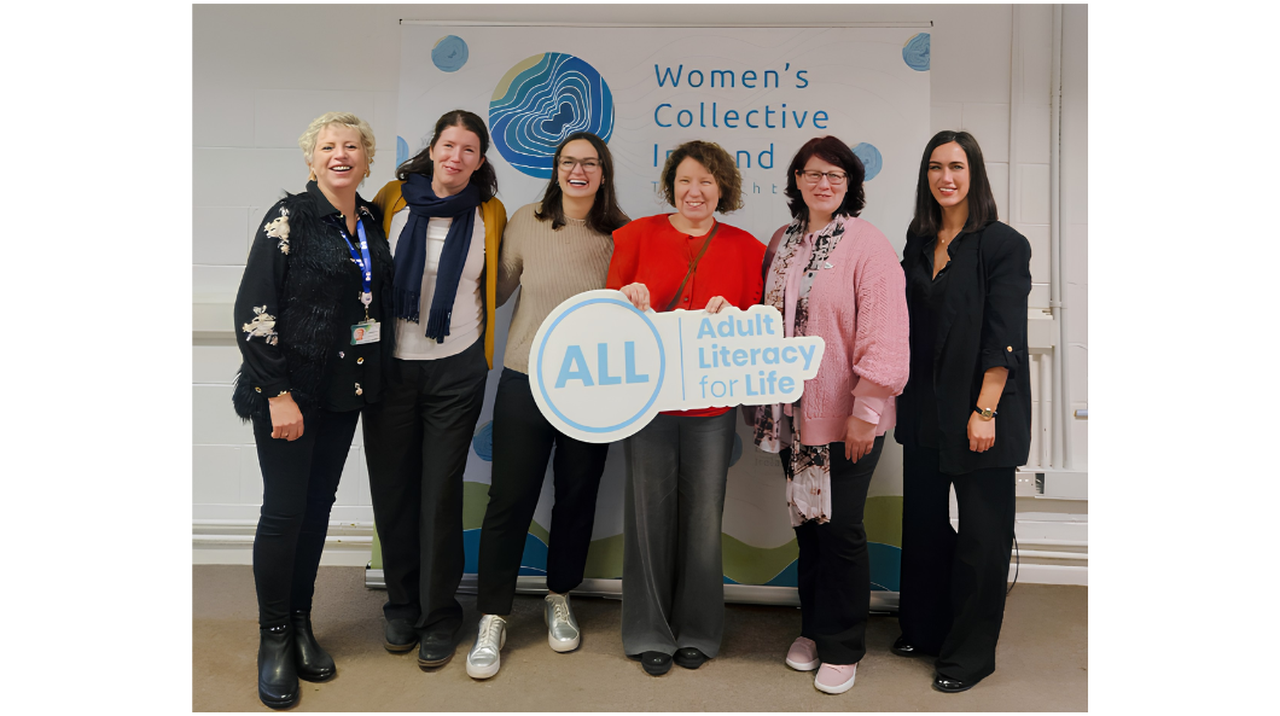 Six smiling women stand together holding a 